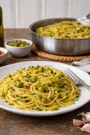 pasta pan of aglio e olive, white plate in front on a wood counter