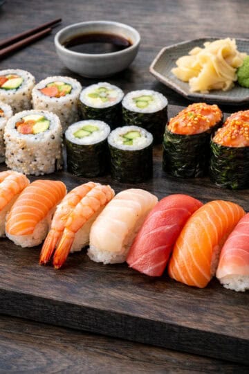 Easy homemade sushi basics featuring simple rolls and nigiri with salmon, tuna, shrimp, and cucumber on a dark oak butcher block.