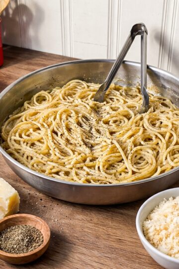 cacio e pepe pasta on a wood counter displayed in a rounded apsta pan