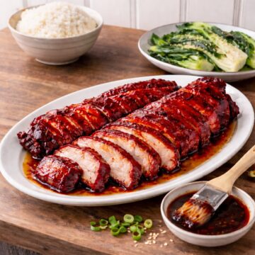 sliced char sui on a platter, bowl of rice and sauteed bok choy on wood countetop