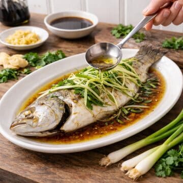 steamed whole fish on a platter, aromaticws and hot oil being pourd on top