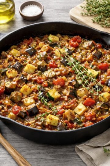 Classic French ratatouille with eggplant, zucchini, tomatoes, and herbs served in a cast iron skillet on a light grey wood surface