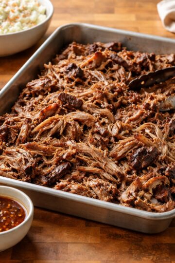 Pulled pork shoulder shredded and ready to serve on a butcher-block countertop, cooked low and slow for tender texture