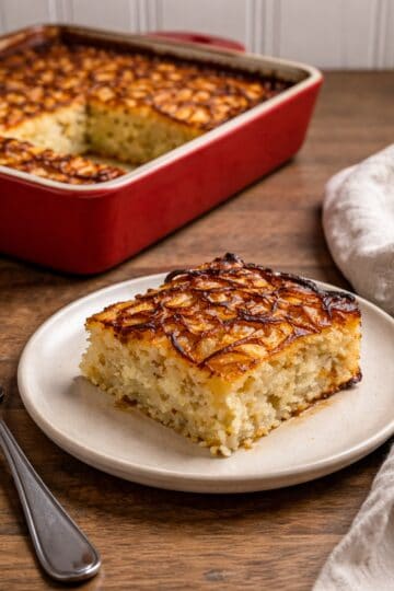 potato kugel in a red cassarole dish, small plate with single serving, fork and napkin on a wood counter top