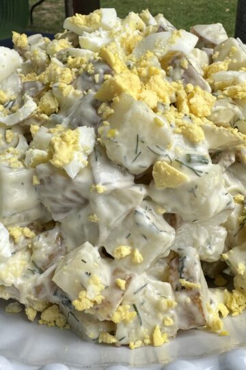 potato salad with fresh dill, hard boiled eggs, creamy dressing in a white bowl