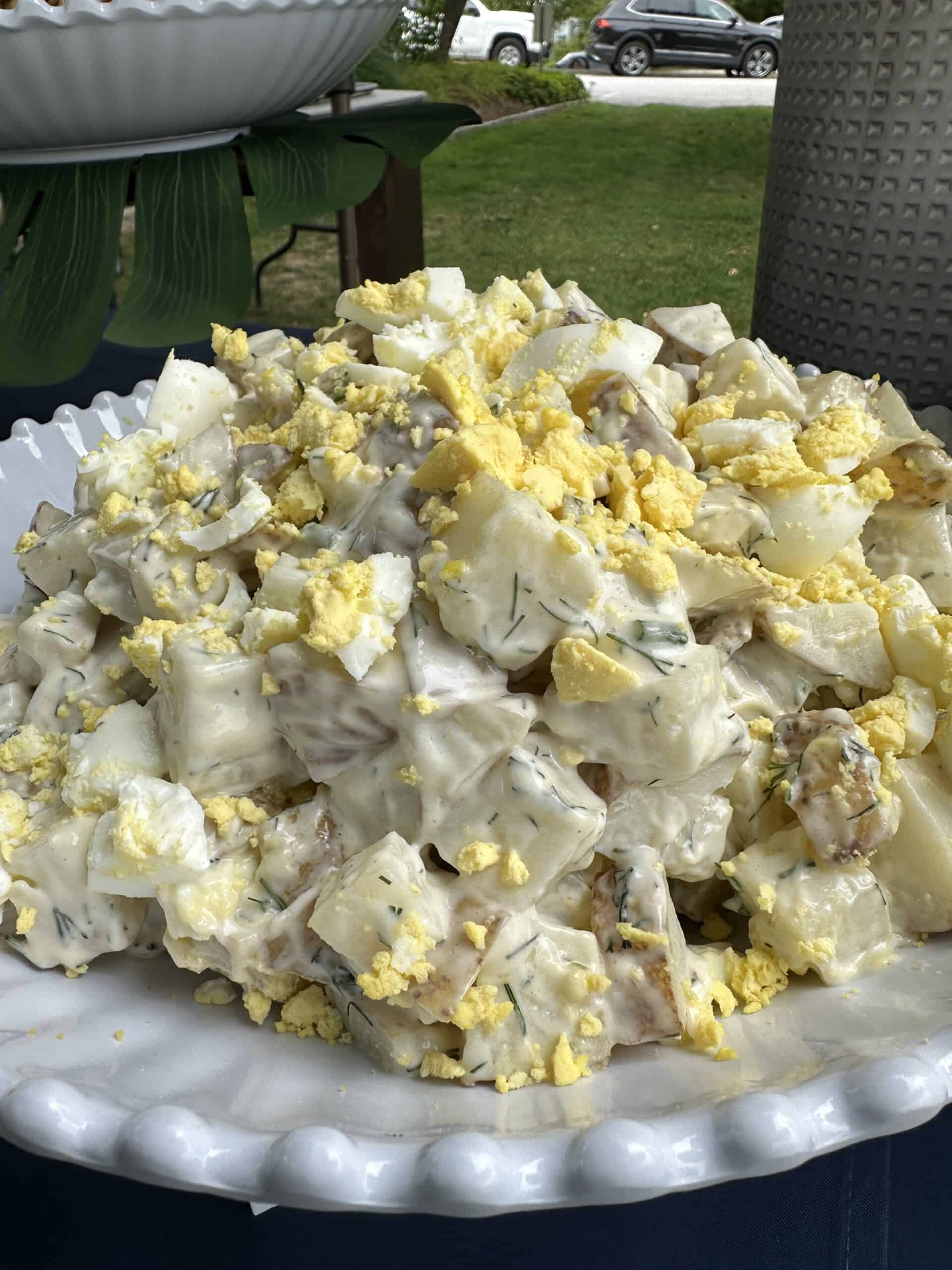 potato sald with fresh dill and hard boiled eggs in a white bowl on a picnic table