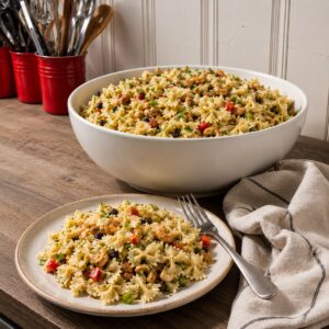 bowtie pasta salad with indain spices, white serving powl and a small plate of salad on a wood counter